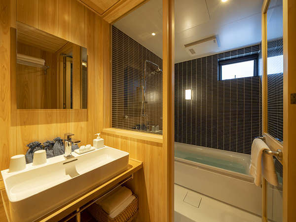 ヒノキ板に囲まれた明るい雰囲気の洗面台、大きな浴槽やシャワーを備えた浴室。