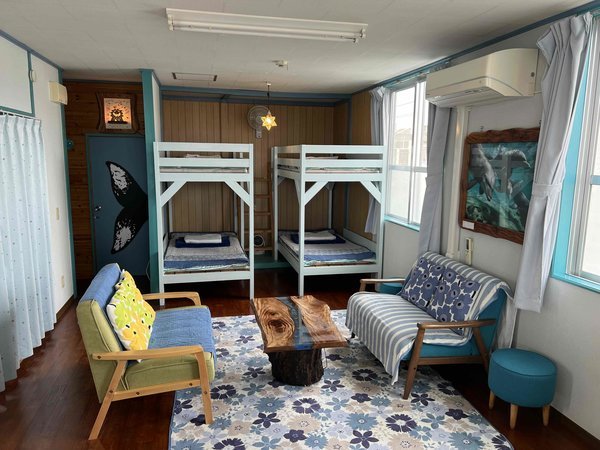 宿主製作の島木の家具がアクセントのリビングルーム。山小屋風２段ベッドがワイルド。もちろん冷暖房完備。