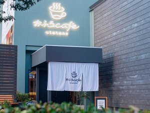 「おふろｃａｆｅ　ｕｔａｔａｎｅ」のおふろcafe utataneのエントランス。のれんとブルーの外壁が目印です。