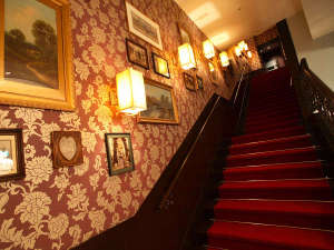 壁面に絵画が飾られ、アンティークな雰囲気漂うホテル内の階段。