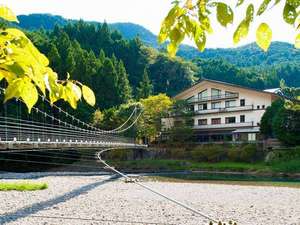 「大露天の宿　わたらせ温泉　ホテルやまゆり」の『やまゆりと吊り橋』川のそばに立つ山小屋風の建物です