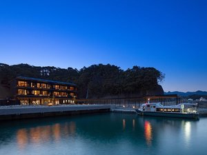 「碧き島の宿　熊野別邸　中の島」の水面に映る明かりが幻想的な送迎船が着岸する南東面の外観。