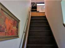【階段】シングル洋室など客室3部屋がある2階への階段（手すり付）。パウル・クレーの絵を観ながら。