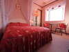 大きな出窓とベッドを囲む白のレースカーテンと花柄の赤が鮮やかなフリルのバッドカバーで優雅さを演出。